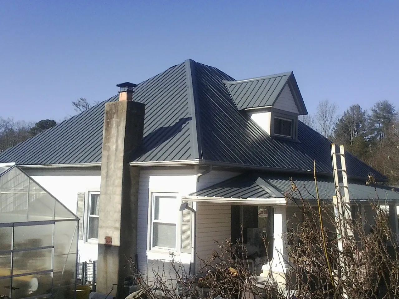 Dark blue standing seam metal roof on a white farmhouse with dormer — Slate & Tile Roof Repair by Roofing Brothers in Leon