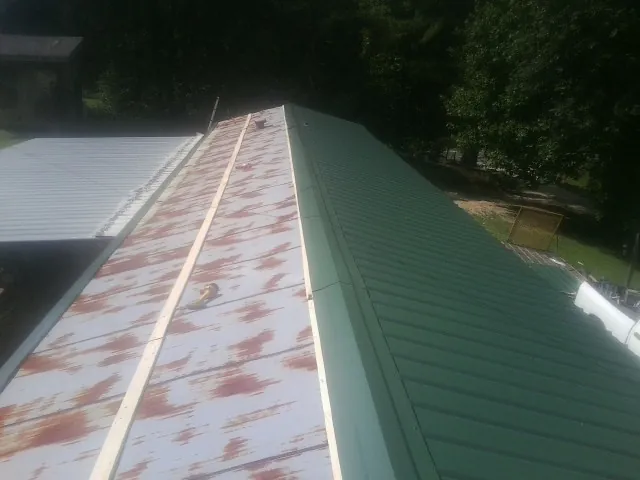 Old rusted panels beside newly installed green metal roofing — Wind Damage Roof Repair by Roofing Brothers in Leon