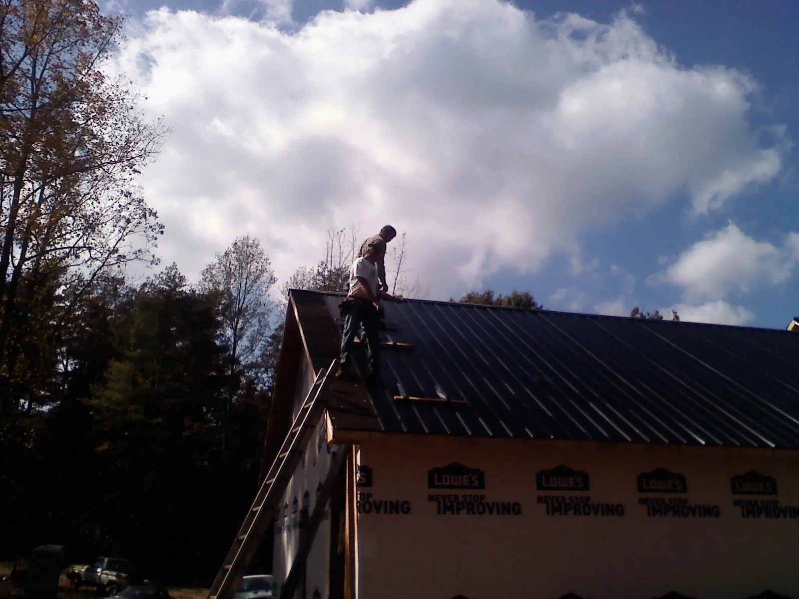 Roofer fastening dark metal panels high against a cloudy sky, from a Roof Inspection job in Leon