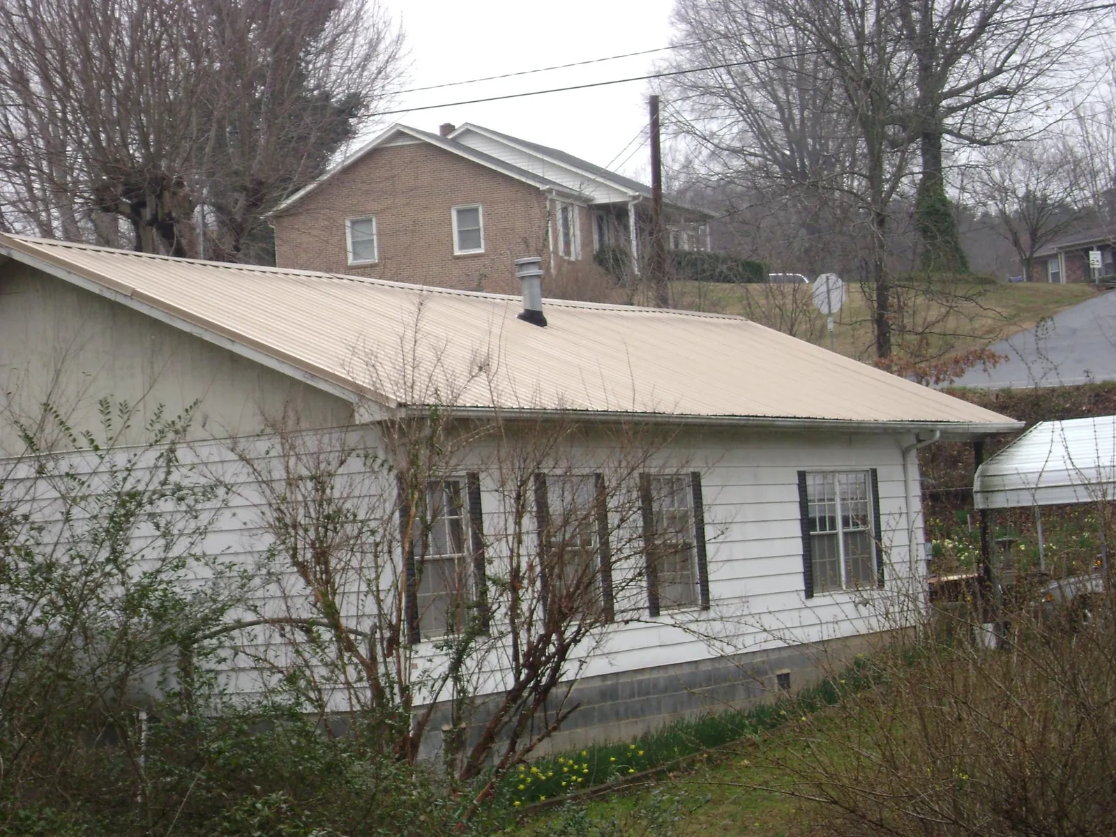 Tan metal roof on a white sided house set into a hillside — Commercial Roofing by Roofing Brothers in Leon